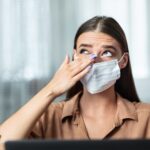 Woman in facemask rubbing her eye